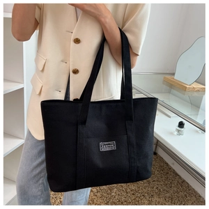 Detail shot of a black canvas tote bag with fashion label shown in a lifestyle setting