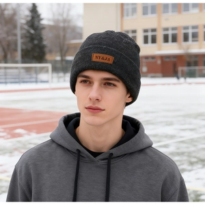 Detail of dark grey winter beanie with brown leather brand tag and knitted texture