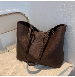 Detail of dark brown tote bag in pebbled leather texture placed on a soft knit sweater