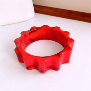 Vue détaillée du bracelet en résine rouge marbrée avec bords ondulés et motifs sombres
