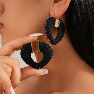 Close-up of black woven heart earrings with golden beads on a model's ear