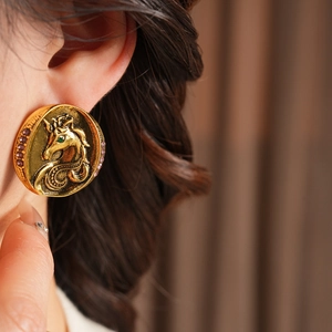 Close-up of vintage golden horse relief earrings with purple and green crystals