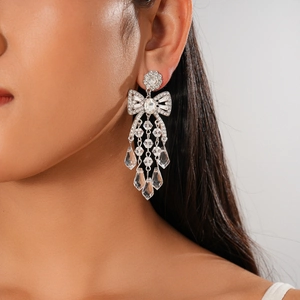 Macro detail of silver-tone bow earrings with rhinestone tassels and waterdrop crystals