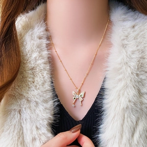 Detail of gold butterfly pendant with green and white zircons on a delicate bead chain