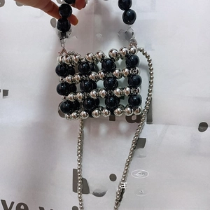 Detail of hand-woven black and silver beaded mini bag with pearl handle and chain strap