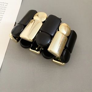 Détail d'un bracelet large élastique géométrique noir et doré aux finitions variées