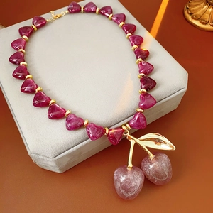 Detail of red heart cherry pendant with golden leaves on a soft jewelry box surface