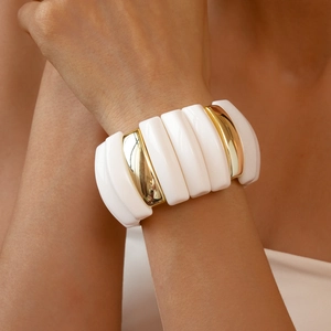 Detail of chunky white acrylic and polished gold metal link bracelet on a model's wrist