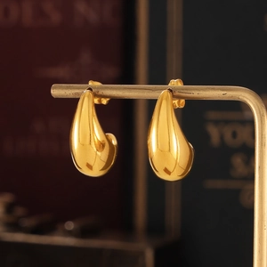 Polished gold crescent hoop earrings displayed on a vertical metal jewelry stand