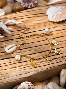 Detail of a golden ocean-themed bracelet with shell, starfish, and pearl charms on wood