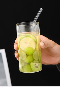 Detalle de vaso de borosilicato estriado con pajita, rodajas de fruta fresca y cubitos de hielo