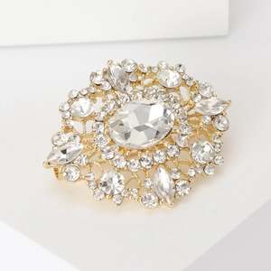 Close-up of golden vintage oval rhinestone brooch with sparkling crystals on white stand
