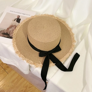 Close-up of a wide-brimmed straw sun hat with frayed edges and a black ribbon bow