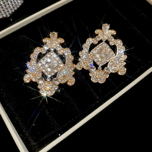 Détail de boucles d'oreilles dorées avec cristaux carrés dans un écrin en velours