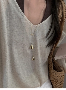 Detail of a gold-plated Y-shaped necklace featuring two liquid-metal style water drop pendants