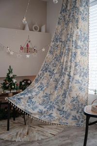 Detail of beige cotton linen curtain featuring blue floral patterns and tassel edges