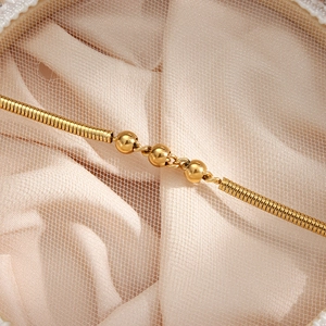 Macro shot of three golden beads on a delicate snake chain necklace with mesh backdrop