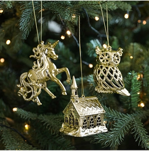 Close-up of golden unicorn, owl and chapel ornaments hanging on a green Christmas tree