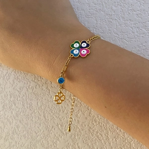 Detail of golden clover evil eye charm bracelet with colorful enamel on female wrist