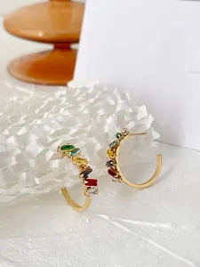 Detailed close-up of C-shaped gold-plated earrings with rainbow gradient square zircons
