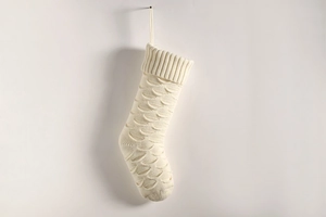 Detail of cream white knitted Christmas stocking with fish scale texture and hanging loop