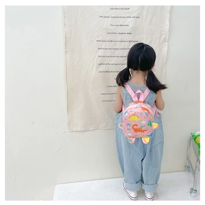 Pink kids dinosaur backpack with 3D fins shown on a little girl in a minimalist setting