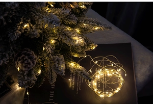 Warm white micro LED copper wire fairy lights on snowy Christmas tree and black books