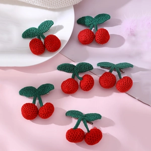 Five handmade knitted red cherry hair clips with green leaves on a soft pink background