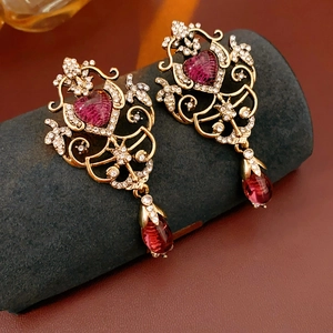 Close-up of vintage gold earrings with heart-shaped purple stones and teardrop crystals