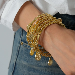 Detail of bohemian gold metal bangles with coin pendants and textured wave patterns