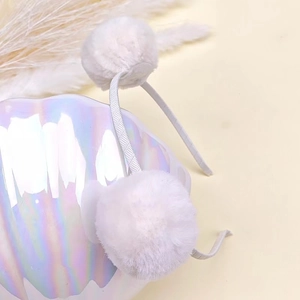 Detail of soft white faux rabbit fur pom poms on a slim headband for children