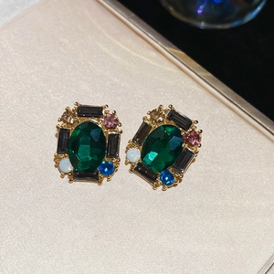 Detailed macro view of vintage gold earrings featuring emerald green stones and rhinestones