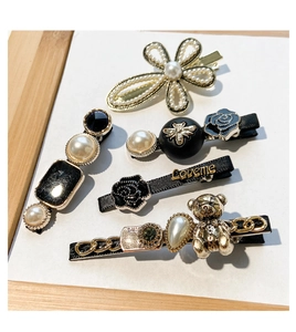 Detail view of 5 pearl and metal hair clips with floral, bee and bear charms in a wooden tray