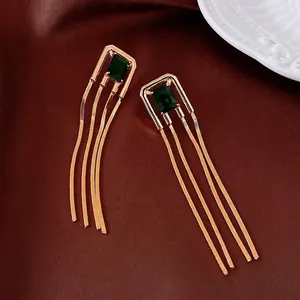 Vintage gold tassel earrings with emerald zircon stones on dark velvet background