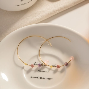 Golden C-shaped stainless steel hoop earrings with colorful beads on a white ceramic plate