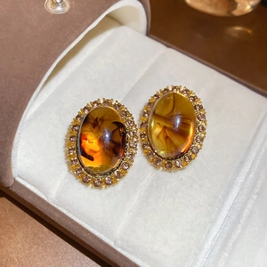 Macro shot of oval amber resin earrings with a sparkling rhinestone halo in a jewelry box