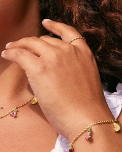 Details eines Goldschmuck-Sets mit bunten Fruchtanhängern, getragen bei natürlichem Licht