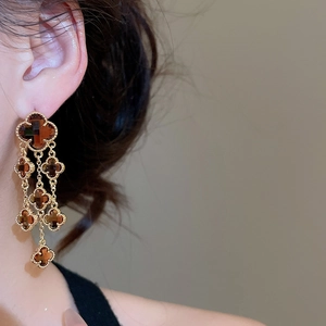 Detailed view of gold-plated long tassel earrings with brown resin clover on a model
