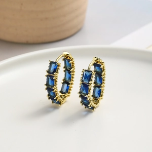 Chic gold hoop earrings with rectangular blue zircon stones on a white ceramic tray