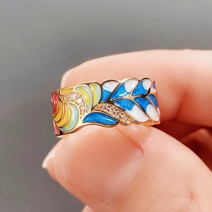 Macro shot of gold ring with vibrant blue and yellow enamel wave patterns and micro diamonds