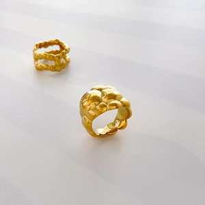 Close-up of a gold-plated fluid lava ring with textured relief on a white surface
