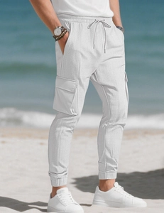 Détail du pantalon cargo blanc avec cordon et poche sur fond de plage ensoleillée