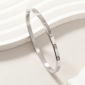 Detailed view of silver stainless steel bangle with rectangular zircon stones on textured stone