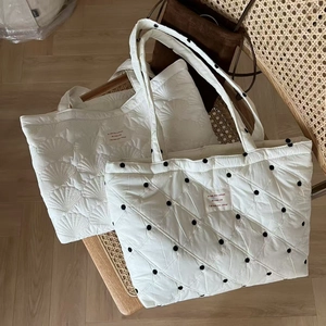 Detail of white quilted tote bags with shell and polka dot patterns on a vintage chair