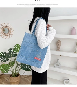 Borsa tote in denim blu con tasca frontale e scritte mostrata su una modella in set minimal