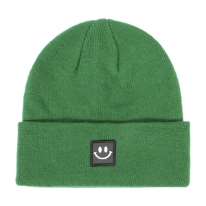 Close-up of a green knitted beanie featuring a black square rubber smiley face patch