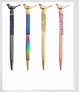 Close-up of metal pens with bird carvings and transparent barrels filled with glitter