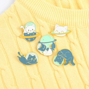 Detailed view of five space-themed cat enamel pins pinned on a yellow knitted sweater
