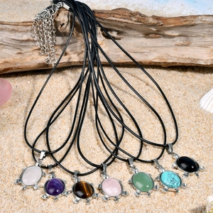 Colliers pendentifs tortue en pierre naturelle avec cordons noirs sur fond de plage