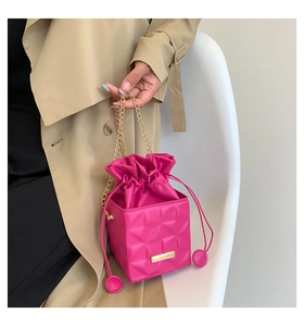 Close-up of fuchsia quilted bucket bag with golden chain and cube texture detail
